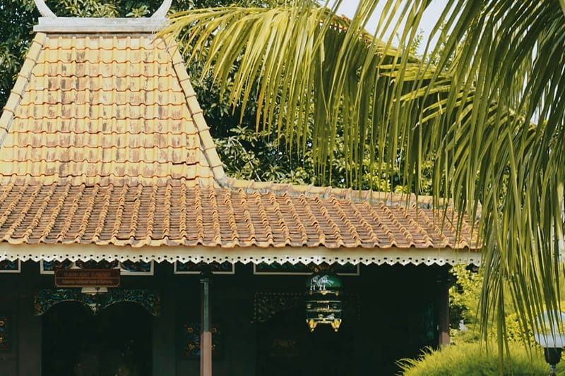 Rumah joglo bertiang kayu dengan atap genteng di antara pepohonan.